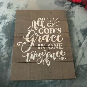 Brown/grey decorative wooden sign, “All of God’s Grace in one tiny face.”